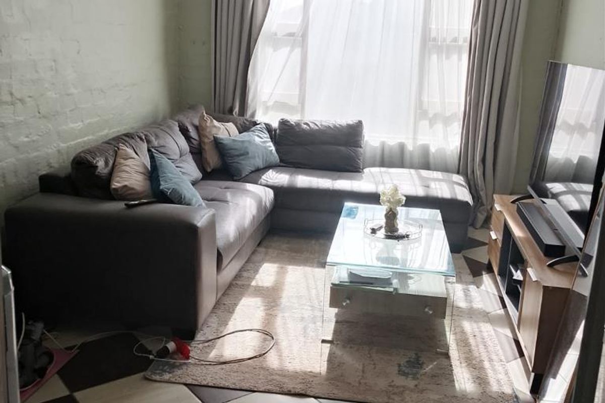 A cozy living room featuring a painted brick wall, large window for natural light, and a distinctive checkered tile floor.
