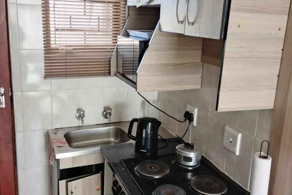 Compact kitchen featuring built-in cabinetry, a stainless steel sink, and an integrated electric hob and oven with tiled splashbacks.