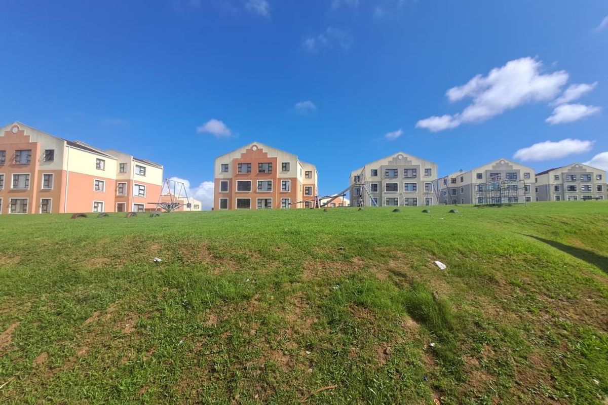 Exterior view of a multi-story apartment complex featuring communal green spaces and playground facilities.