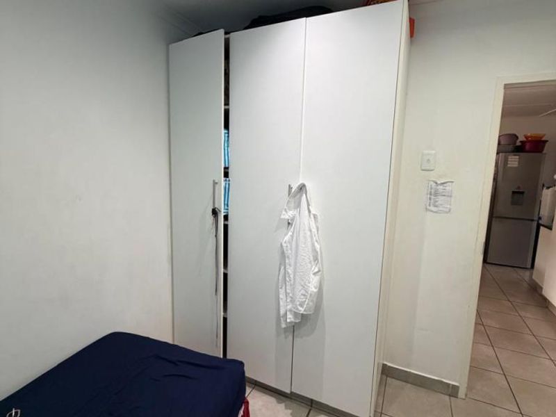 A bedroom featuring tiled flooring, recessed ceiling lighting, and a white built-in wardrobe, with a view into the adjacent kitchen area.