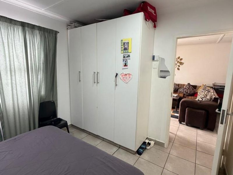 Bedroom featuring tiled flooring, recessed downlights, and a white built-in wardrobe, with a view into the adjacent living area.