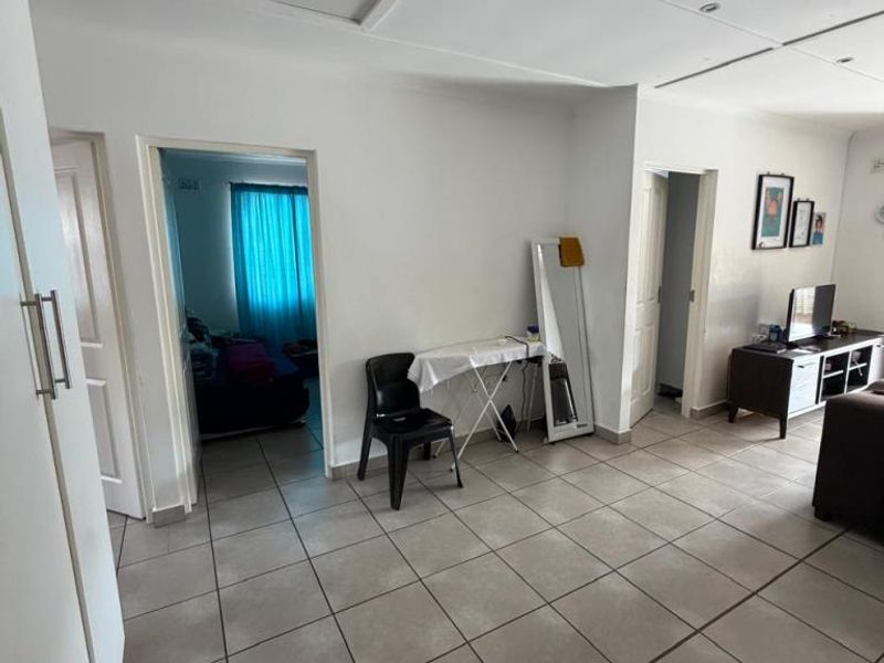 Open-plan living area featuring neutral tiled flooring and recessed ceiling lighting, providing a functional space with access to adjacent rooms.