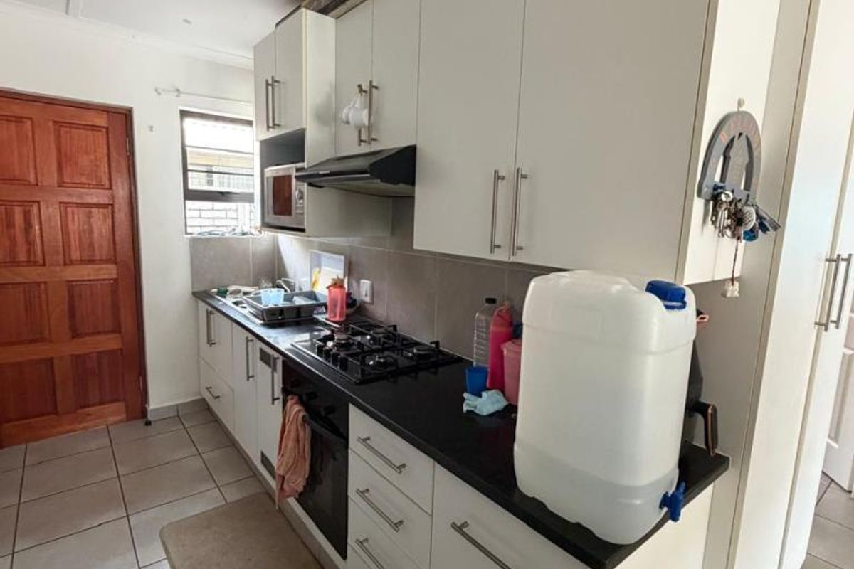 A functional kitchen featuring white cabinetry, dark stone countertops, a gas hob, and an extractor fan, with tiled flooring throughout.