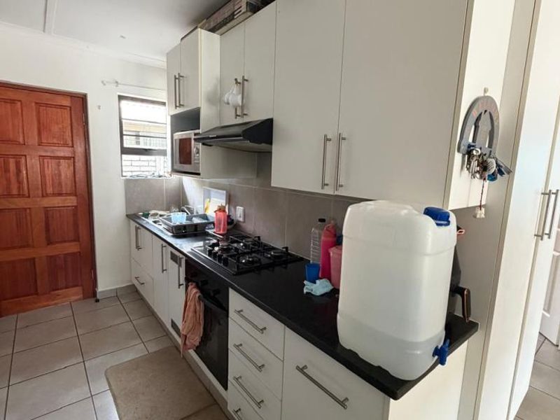 A functional kitchen featuring white cabinetry, dark stone countertops, a gas hob, and an extractor fan, with tiled flooring throughout.