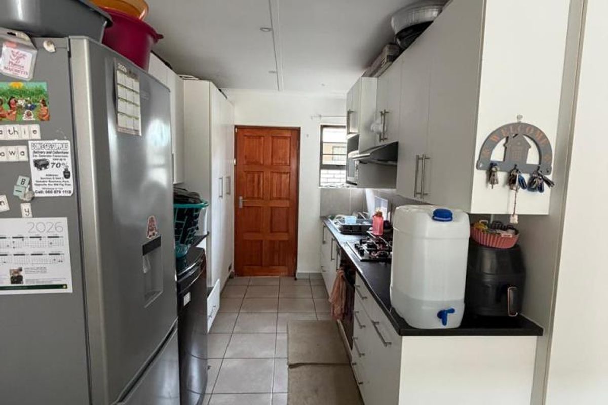 A functional galley-style kitchen featuring white cabinetry, dark countertops, a gas hob with extractor fan, and neutral floor tiles.