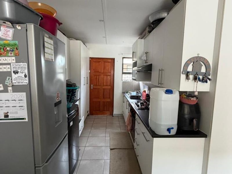 A functional galley-style kitchen featuring white cabinetry, dark countertops, a gas hob with extractor fan, and neutral floor tiles.