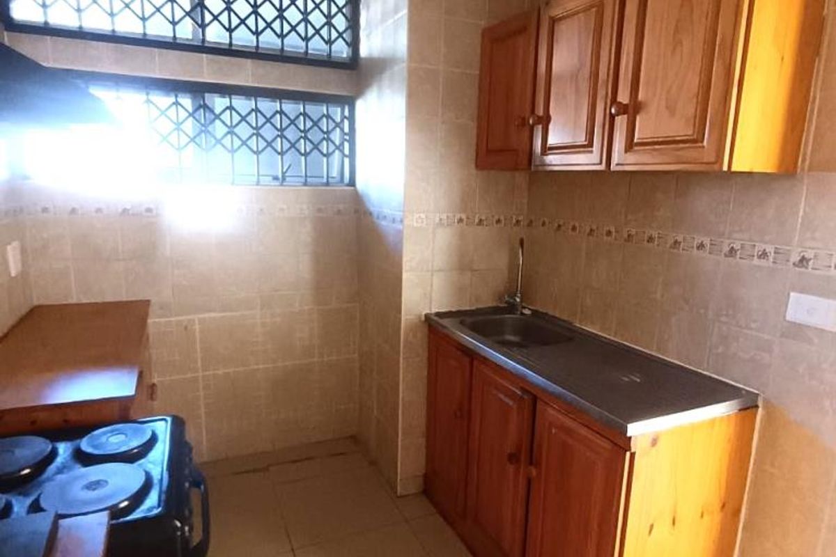A functional kitchen featuring wooden cabinetry, a stainless steel sink, tiled backsplash, and security bars on the windows.