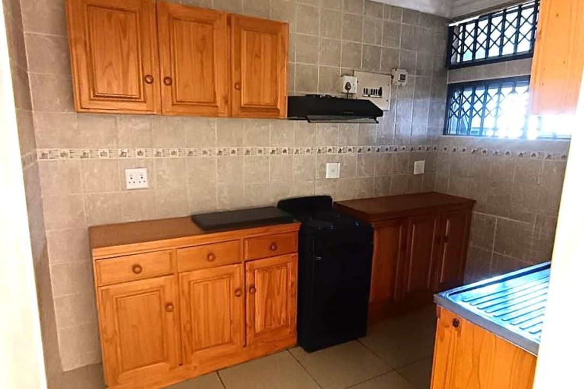 A functional kitchen featuring wooden cabinetry, tiled backsplash, and built-in stove, providing a practical workspace with secure window access.