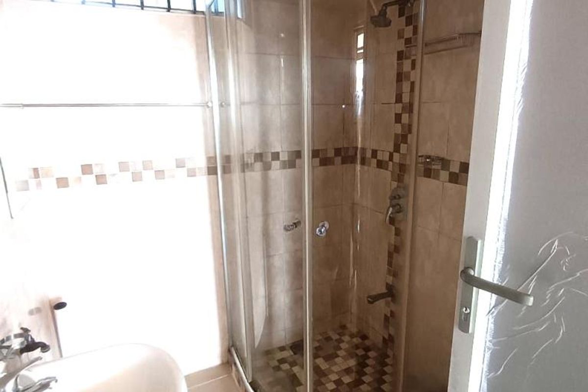 A functional bathroom featuring a pedestal basin and a curved glass shower enclosure with decorative tiled accents and a security window.