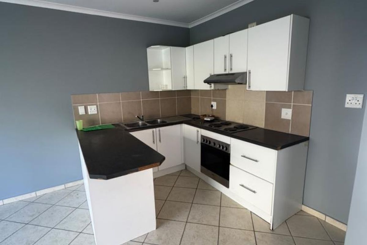 A clean, functional kitchen featuring white cabinetry, dark countertops, built-in oven and hob, tiled backsplash, and neutral tiled flooring.