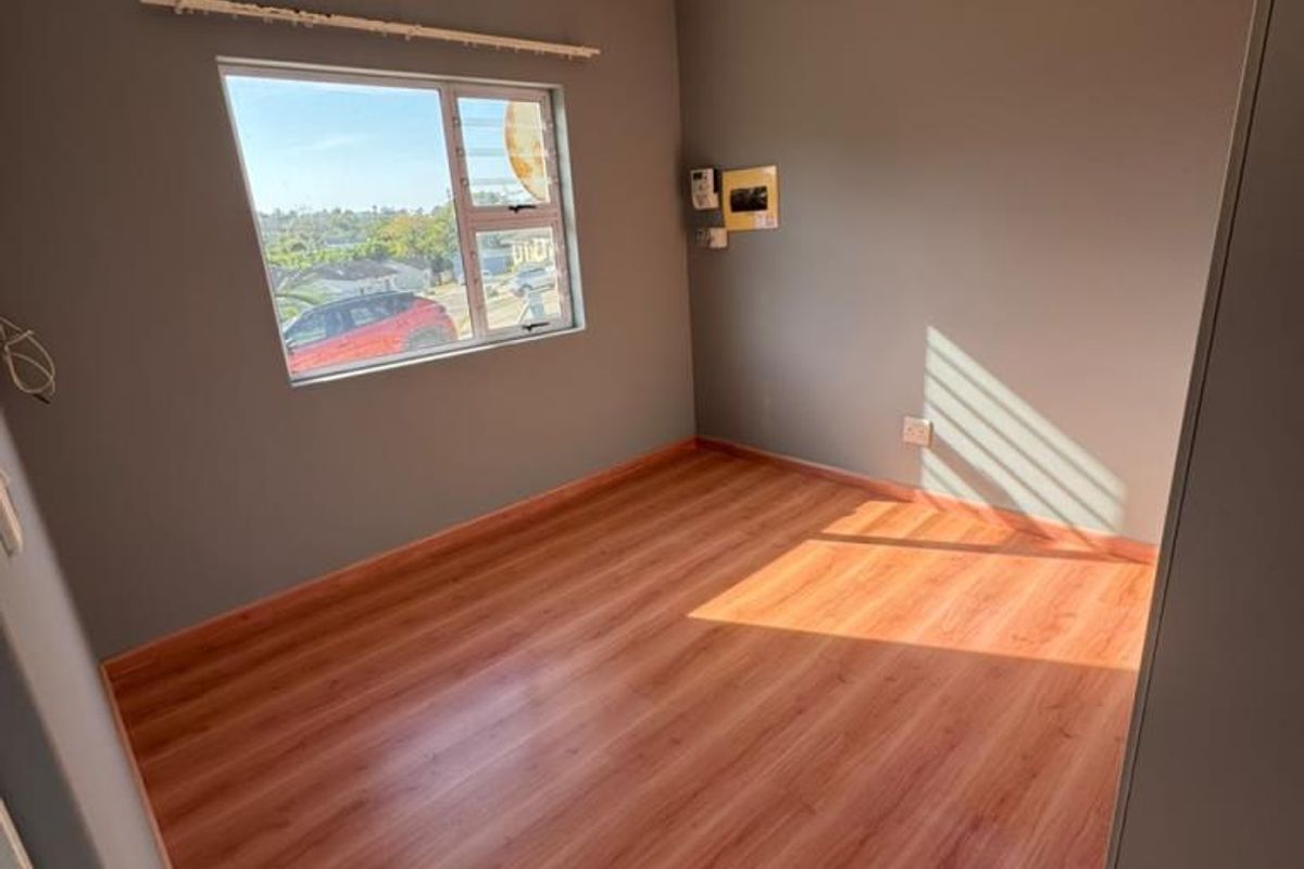 A bright, empty bedroom featuring laminate flooring, neutral grey walls, and a built-in cupboard, offering a clean and versatile space.