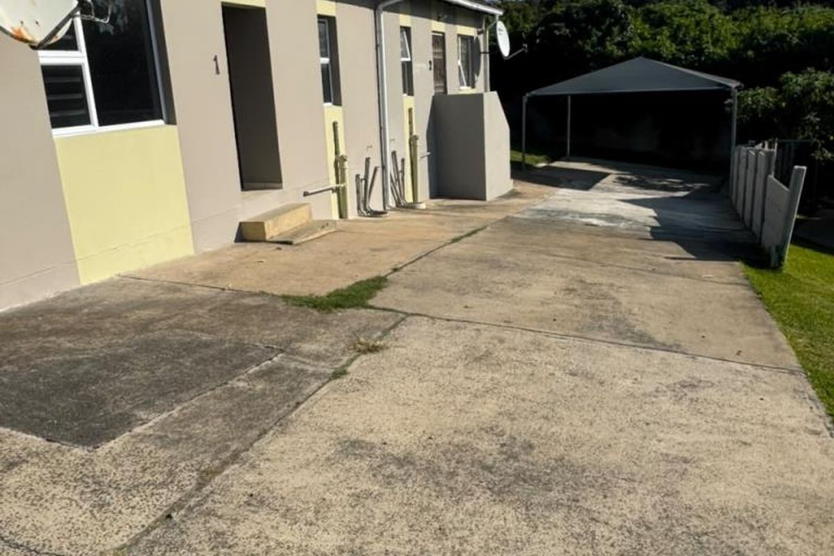 Rear exterior view of the townhouse featuring a concrete driveway, carport, and paved patio area with access to the main building.