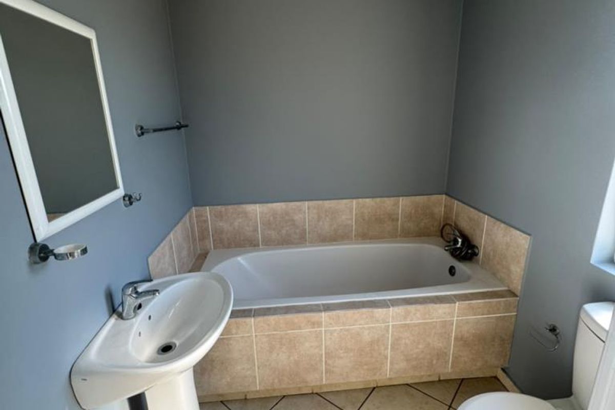 A functional bathroom featuring a pedestal basin, built-in bathtub with tiled surround, and ceramic floor tiles.