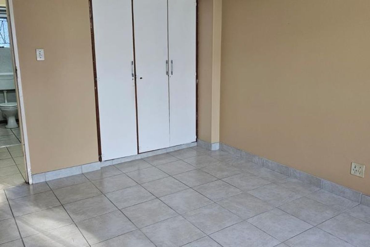 An empty bedroom featuring neutral wall paint, ceramic floor tiles, a ceiling fan, and a built-in wardrobe with white doors.