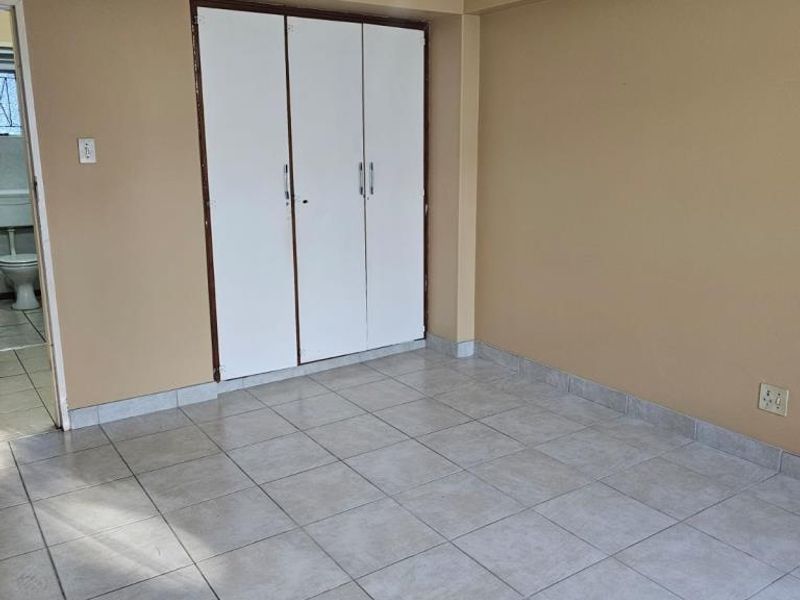 An empty bedroom featuring neutral wall paint, ceramic floor tiles, a ceiling fan, and a built-in wardrobe with white doors.