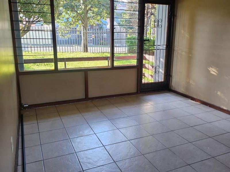 An empty living area featuring tiled flooring, a ceiling fan, and large windows with security bars, providing natural light and access to the exterior.