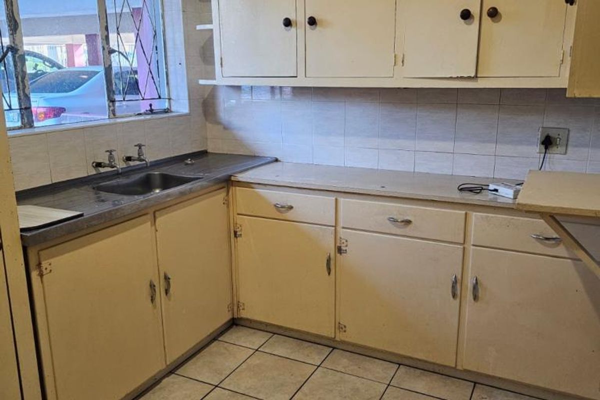 A dated kitchen featuring original cabinetry, tiled flooring, and a stainless steel sink, offering significant potential for modernization and renovation.