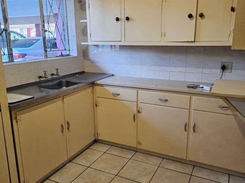 A dated kitchen featuring original cabinetry, tiled flooring, and a stainless steel sink, offering significant potential for modernization and renovation.