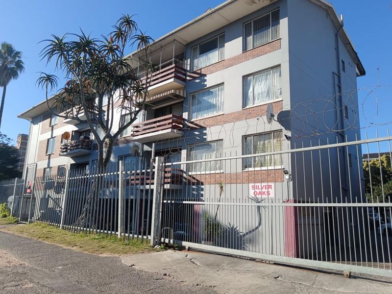 Exterior view of the Silver Oaks apartment complex featuring a multi-story brick and painted facade with balconies and secure perimeter fencing.