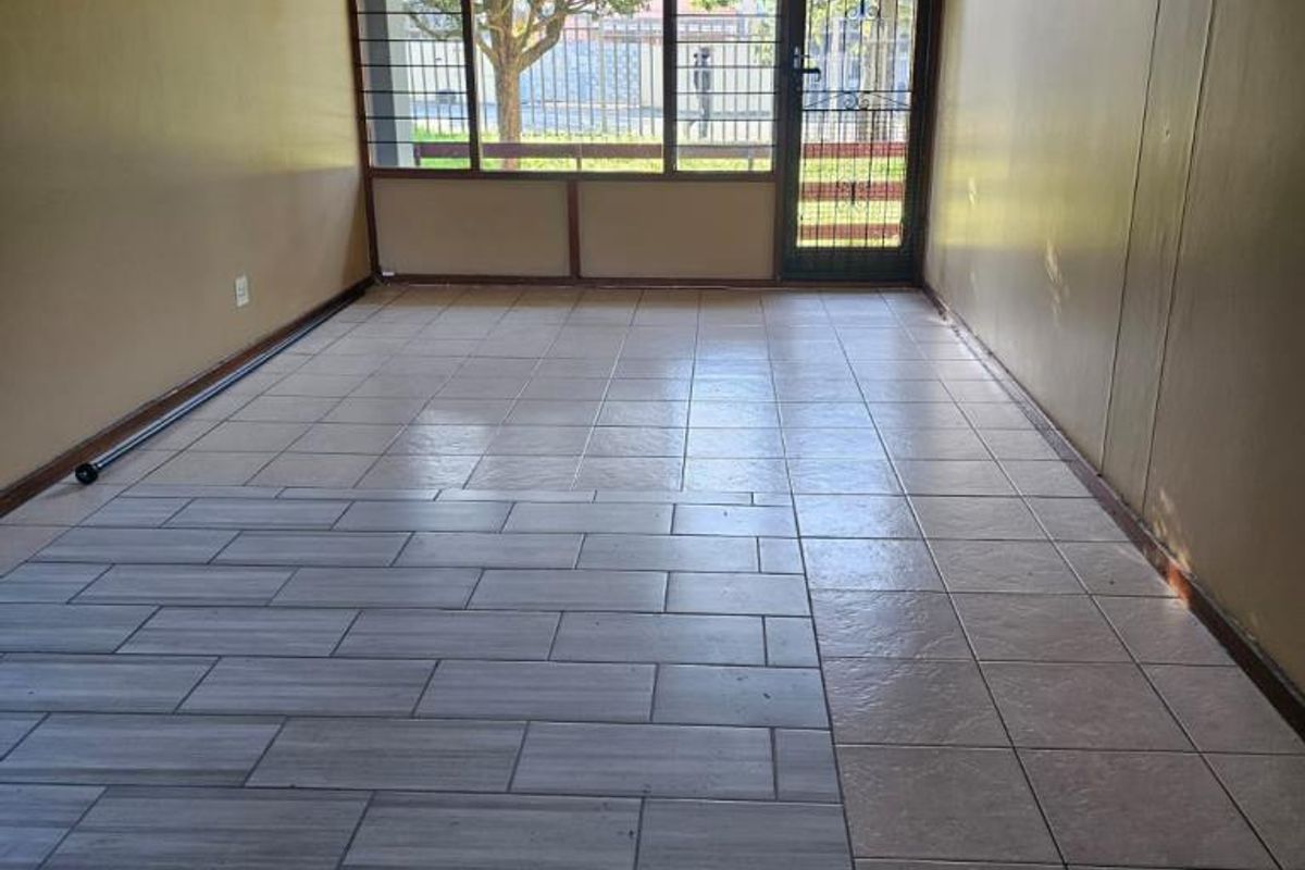 An empty living area featuring tiled flooring, a ceiling fan, and a security gate leading to the exterior.