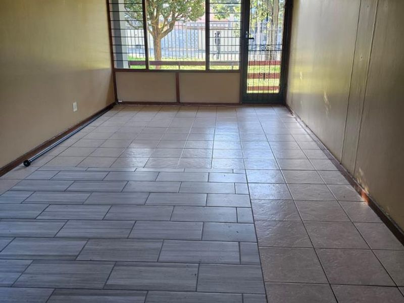 An empty living area featuring tiled flooring, a ceiling fan, and a security gate leading to the exterior.