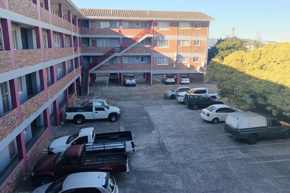 Exterior view of an apartment complex featuring a brick facade, external staircase, and a paved parking area.