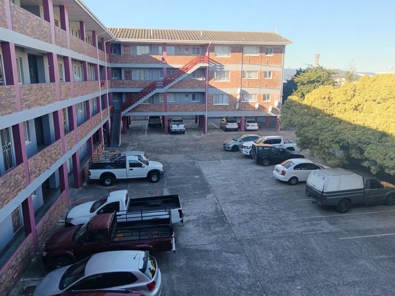 Exterior view of an apartment complex featuring a brick facade, external staircase, and a paved parking area.