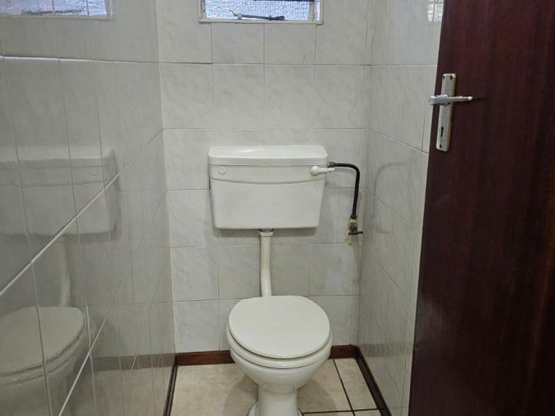 A compact, dated guest toilet featuring ceramic wall and floor tiles with a small obscured glass window.