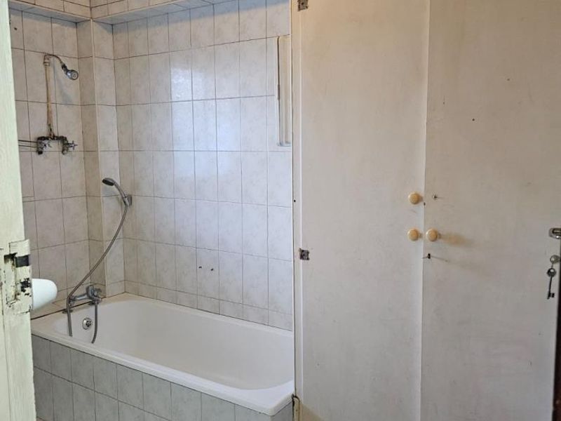 A dated bathroom featuring a built-in bathtub with shower mixer and a large built-in storage cupboard, requiring cosmetic updates to modernize the space.