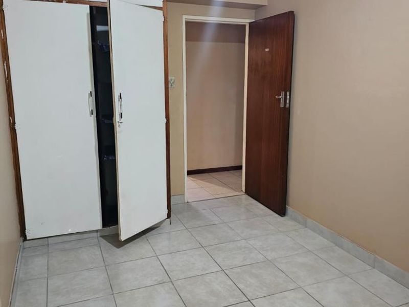 A vacant bedroom featuring neutral tiled flooring and a built-in wardrobe with overhead storage compartments.