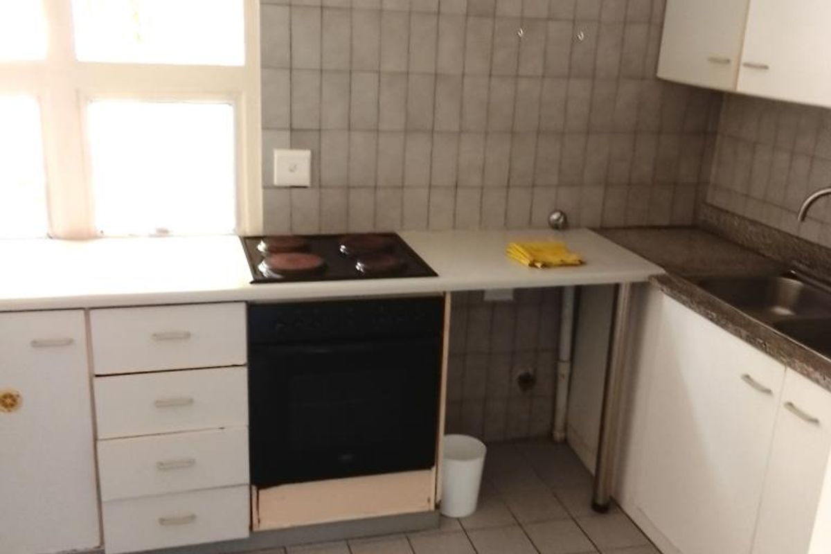 A functional kitchen featuring white cabinetry, a built-in oven with hob, tiled flooring, and a tiled splashback area.
