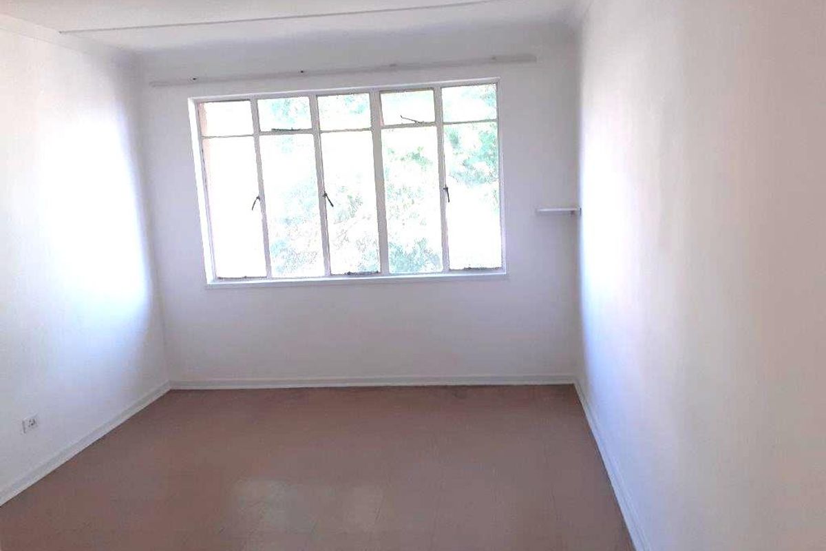 A bright, empty bedroom featuring tiled flooring and a large multi-pane window, offering a blank canvas for personalization.