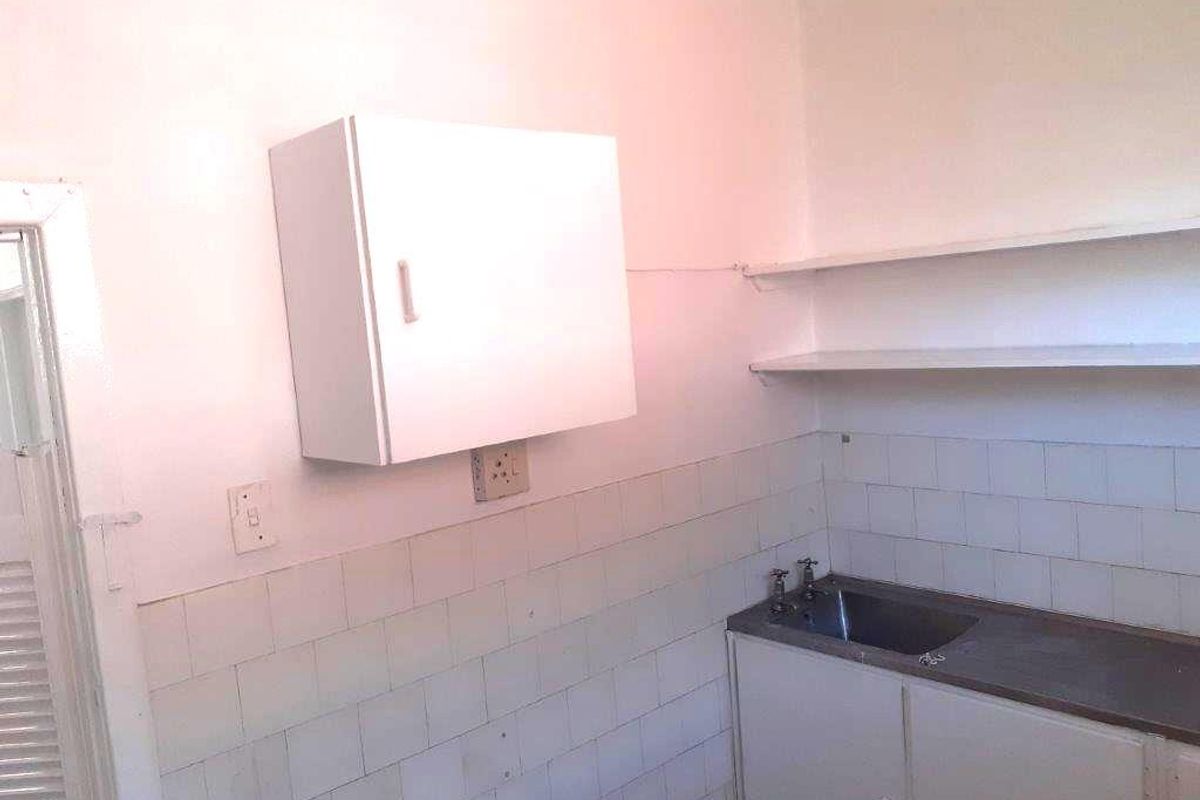 A functional scullery or utility area featuring a stainless steel sink, tiled splashback, and basic wall-mounted and base cabinetry.