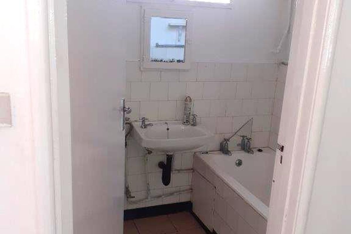 A compact bathroom featuring a bathtub, wall-mounted basin, and an electric water heater, requiring cosmetic updates to modernize the space.