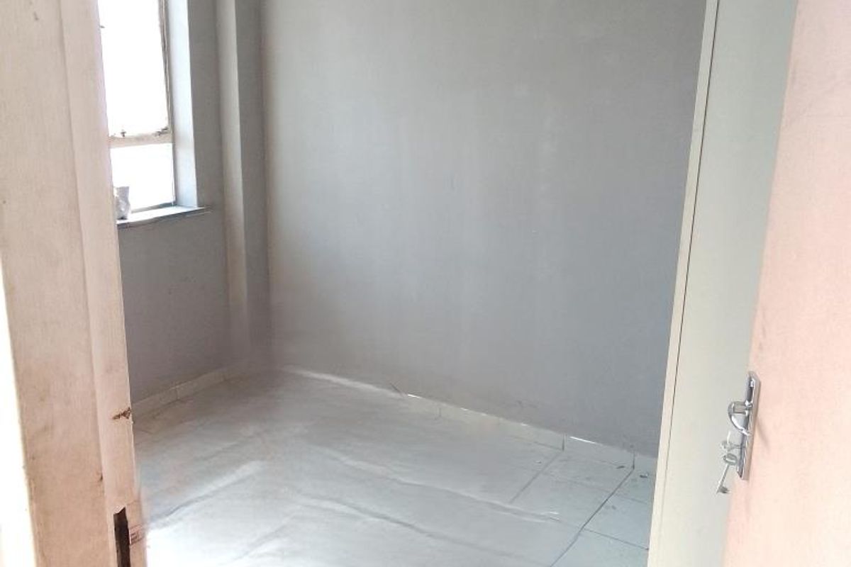 An empty bedroom featuring tiled flooring and a window, presenting a blank canvas ready for renovation or staging.