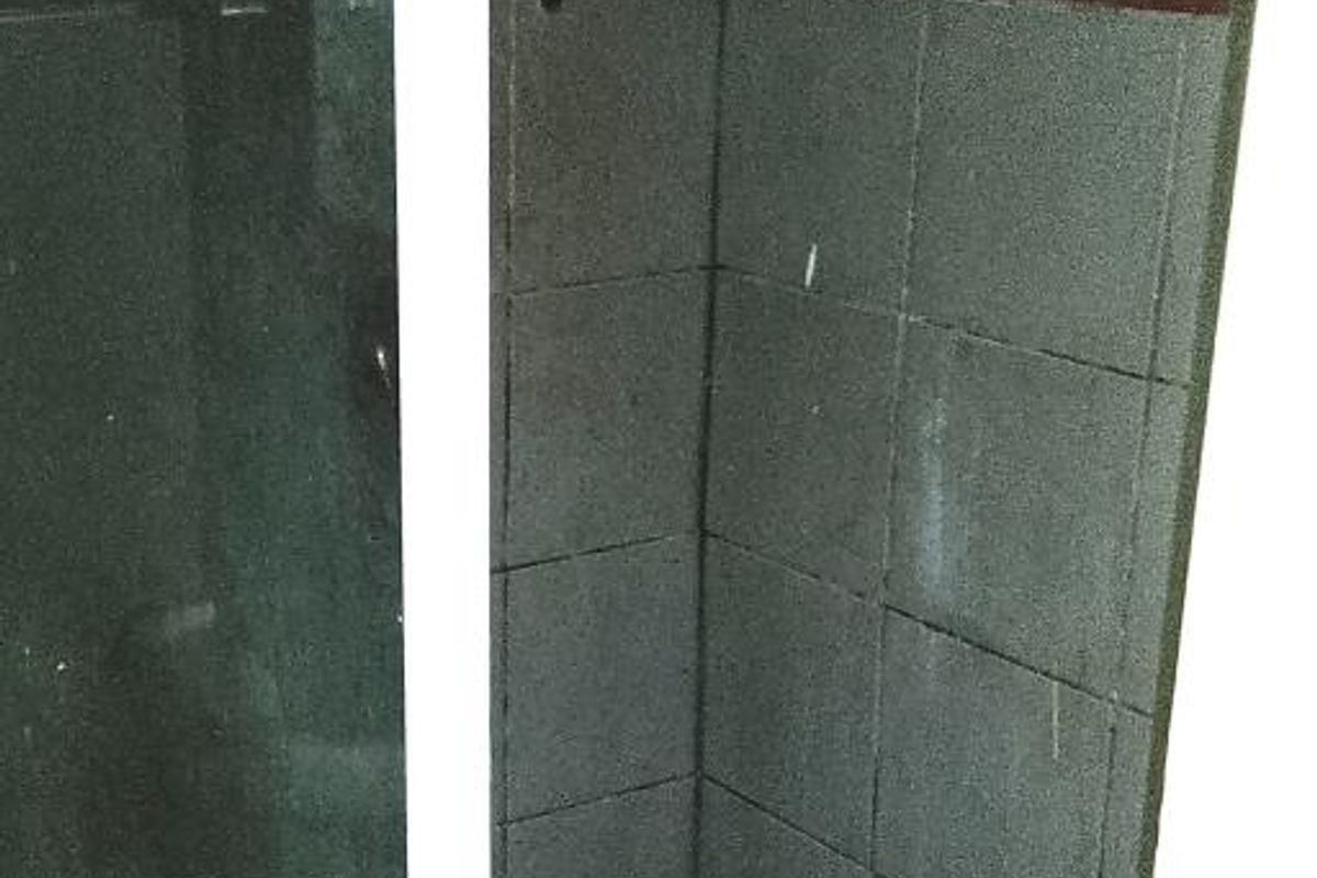 A compact shower stall featuring dark grey tiling and a glass enclosure, requiring maintenance and cosmetic updates to improve its overall condition.