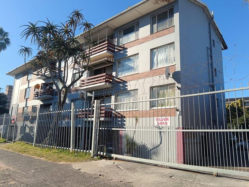 Exterior view of the Silver Oaks apartment complex, featuring multi-story residential units with balconies, security fencing, and razor wire perimeter protection.