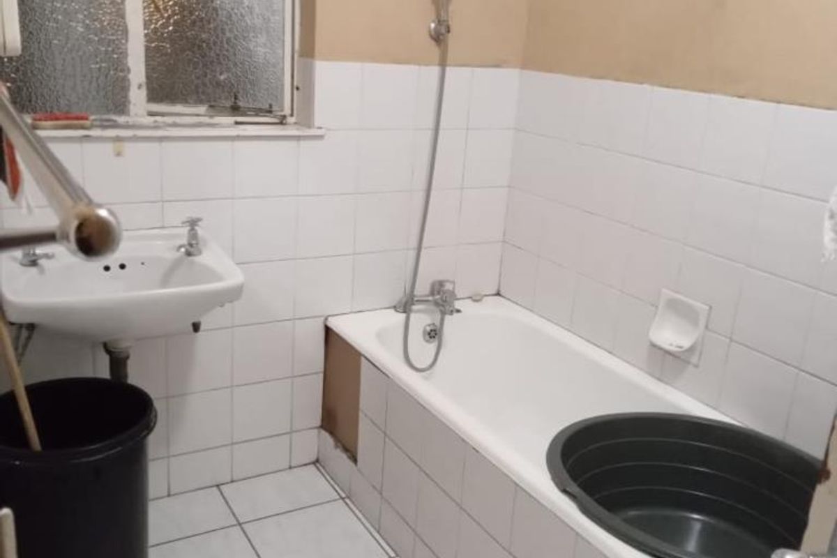 A dated bathroom featuring a bathtub with a handheld shower, a wall-mounted basin, and tiled finishes, currently requiring cosmetic updates and repairs.