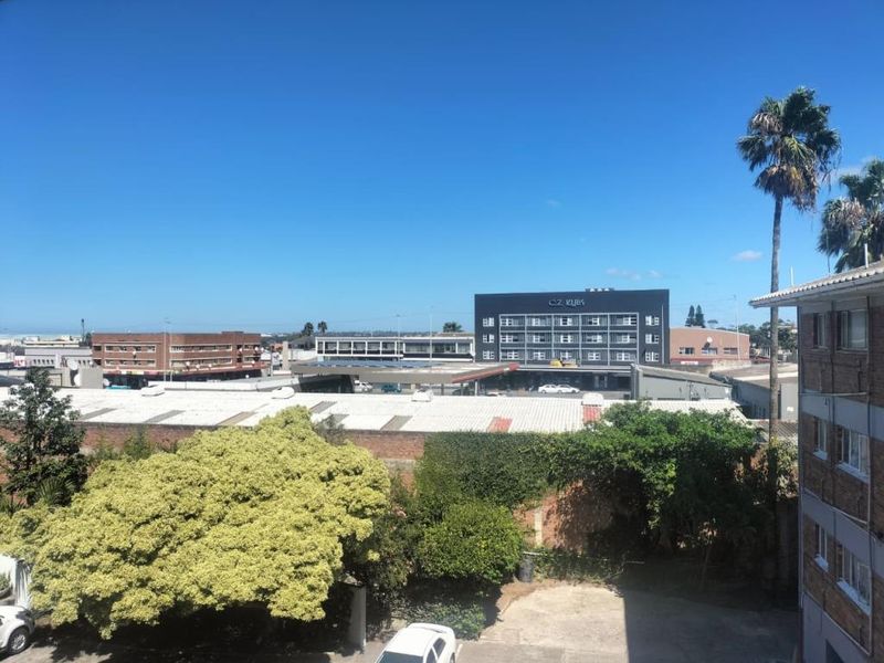 An elevated view overlooking the surrounding urban neighborhood, featuring nearby commercial buildings and mature trees under a clear blue sky.