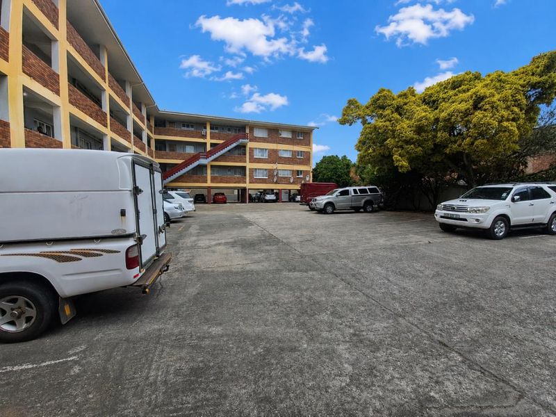 Exterior view of the apartment complex showing the rear parking area and multi-story brick building facade with external staircase access.
