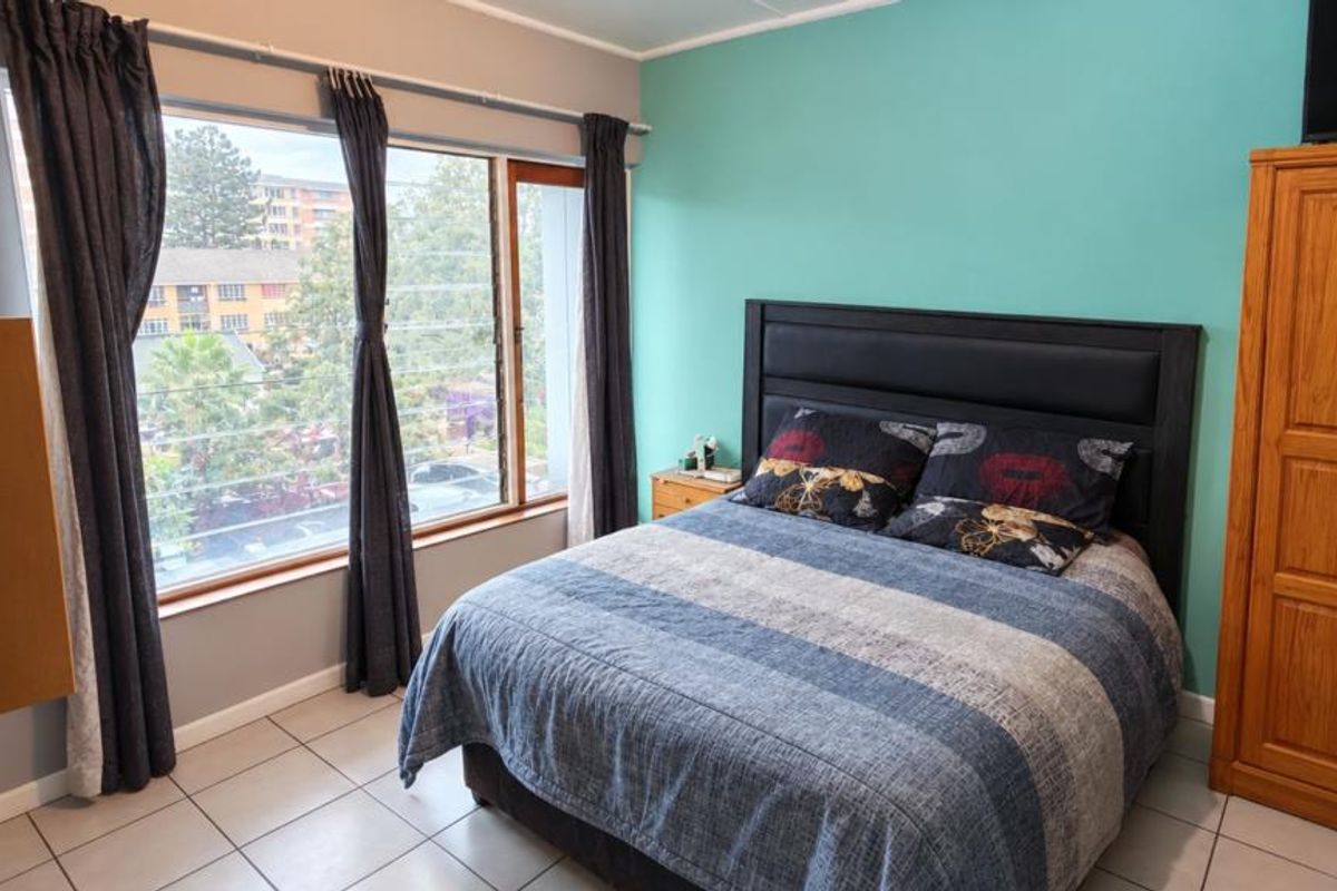 A bedroom featuring tiled flooring, a large window with natural light, and a vibrant teal accent wall.