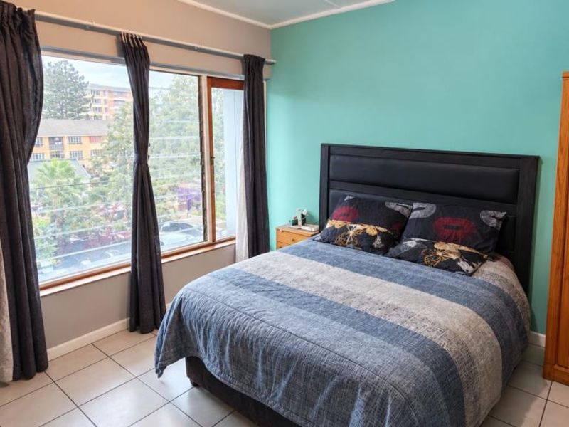 A bedroom featuring tiled flooring, a large window with natural light, and a vibrant teal accent wall.