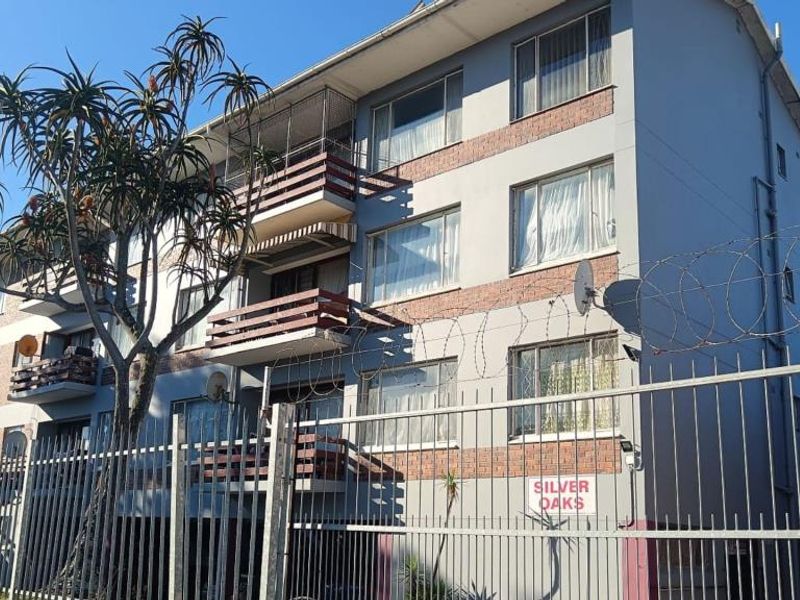 Exterior view of the Silver Oaks apartment building featuring a brick and painted facade, private balconies, and perimeter security fencing with razor wire.