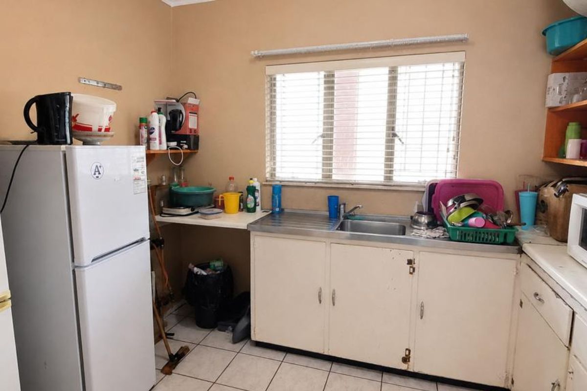 A functional kitchen featuring built-in cabinetry, a stainless steel sink, and tiled flooring, offering potential for modernization and cosmetic updates.