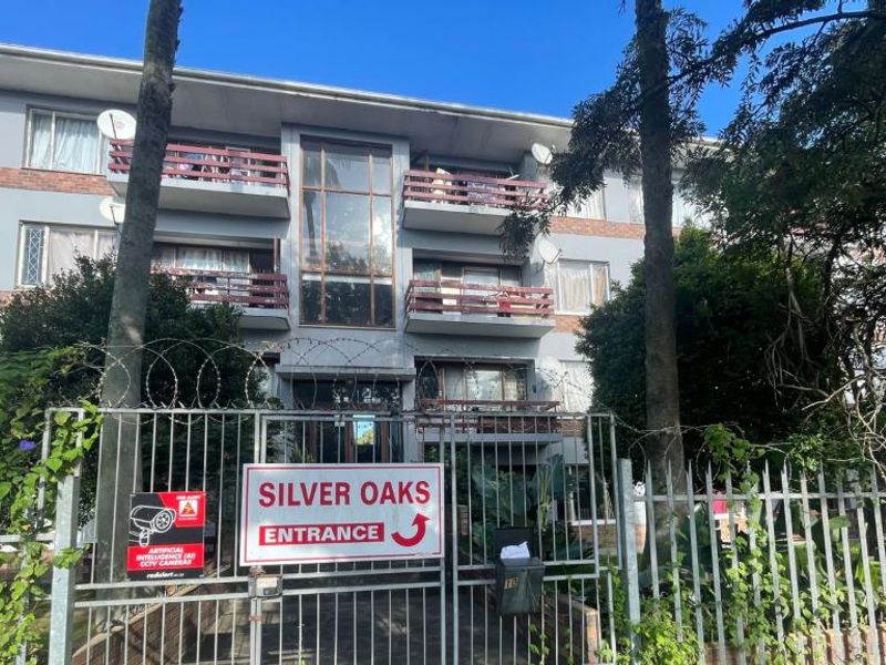 Front exterior view of the Silver Oaks apartment complex, featuring a secure gated entrance, brick facade, and multiple balconies.
