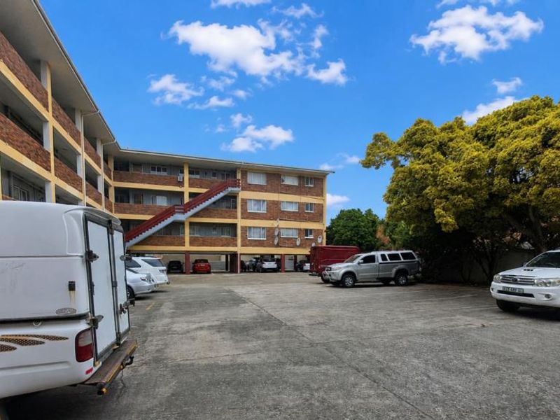 Exterior view of a multi-story apartment complex featuring a brick facade, external staircase, and an open paved parking area.