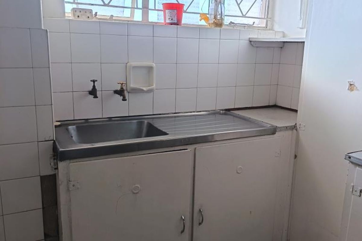 A functional kitchen area featuring a stainless steel sink, tiled splashback, and built-in cabinetry, requiring cosmetic updates to modernize the space.