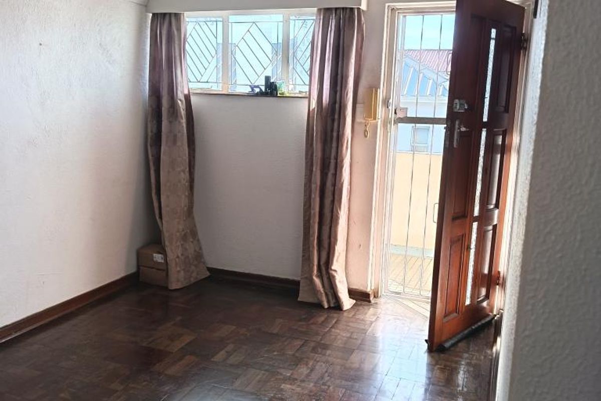 An empty living area featuring original parquet flooring, a timber entrance door with security gate, and window security bars.