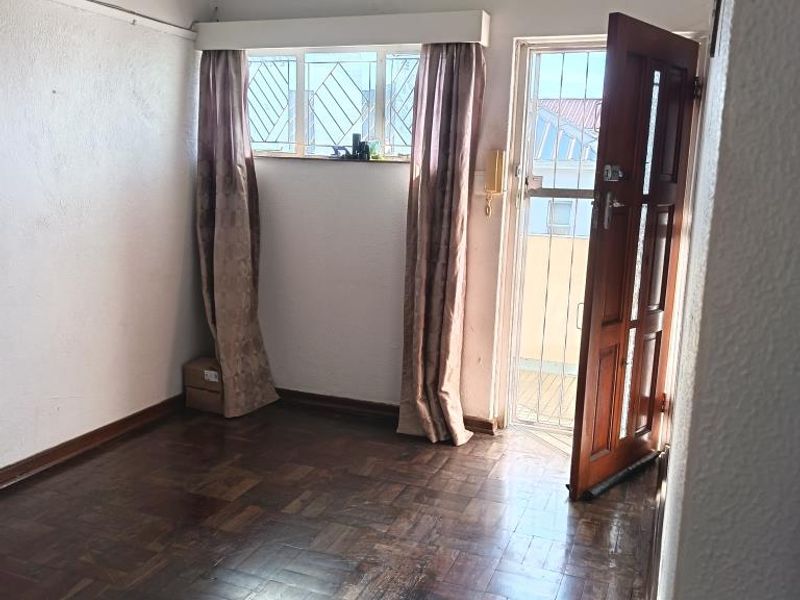 An empty living area featuring original parquet flooring, a timber entrance door with security gate, and window security bars.