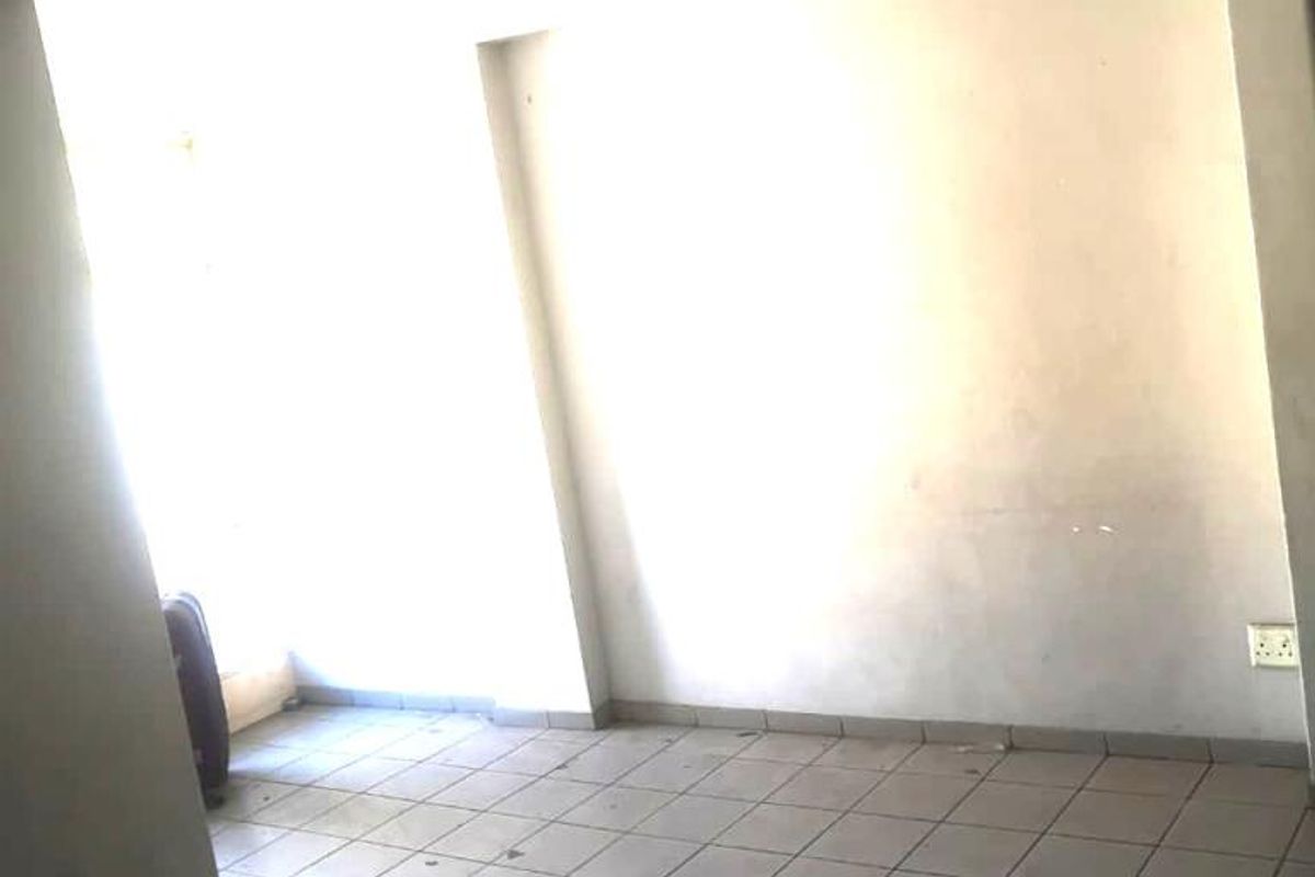 An empty, dated living area featuring tiled flooring and basic lighting, requiring cosmetic updates and repairs to the ceiling and wall finishes.